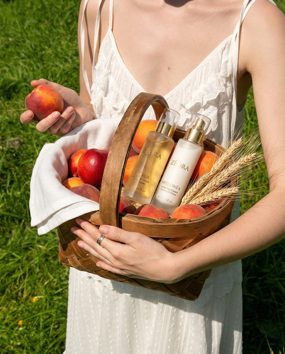 Woman in a white dress holding a woven basket of peaches with two ZÉORA skincare bottles